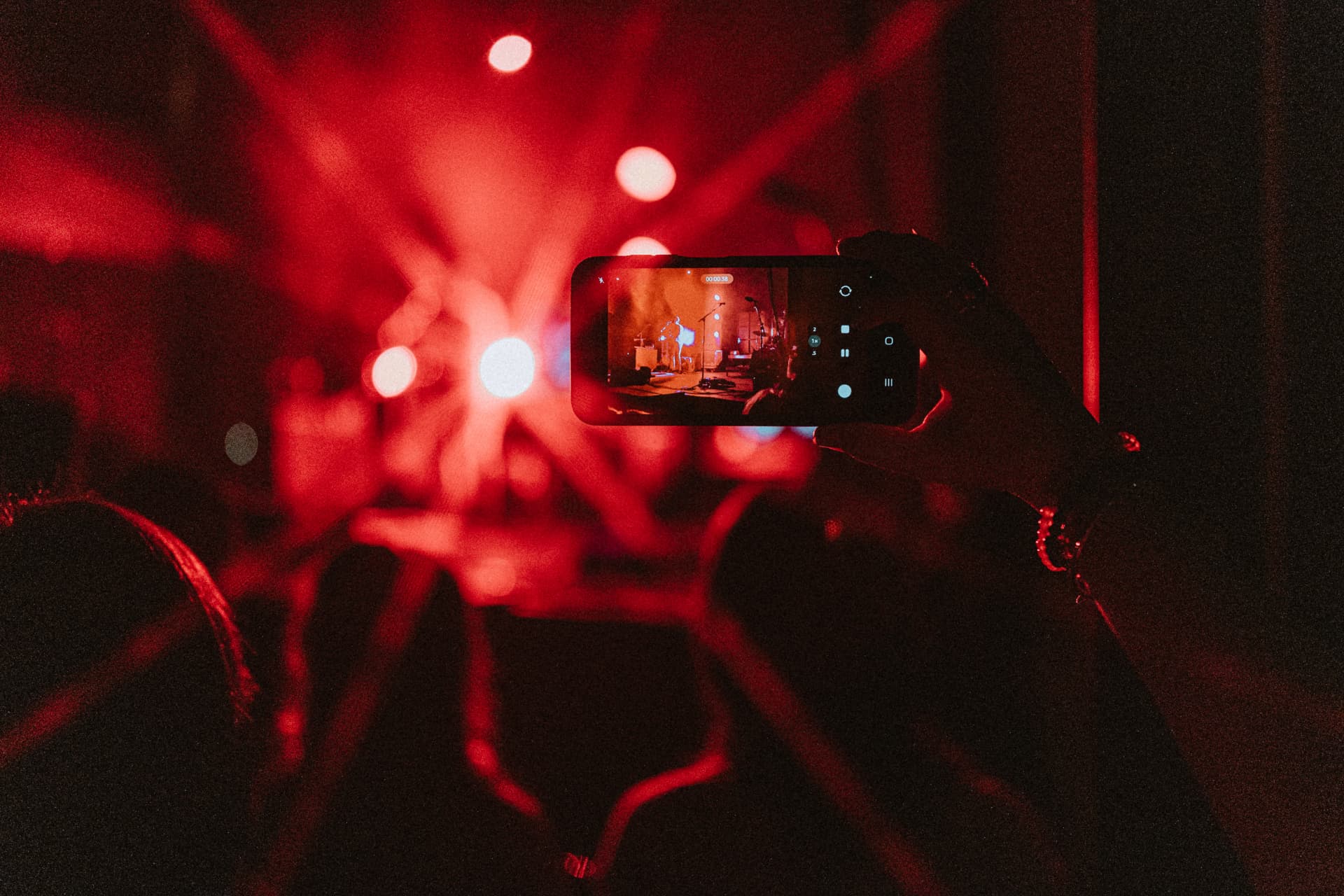 A phone recording a band on stage in the middle of bright red concert lighting