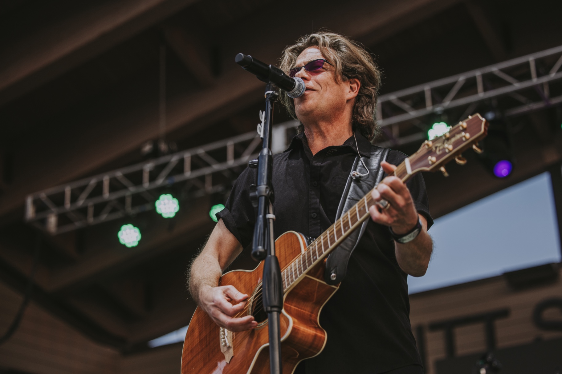 Kory Van Sickle singing and playing acoustic guitar under stage lights at Levitt at the Falls