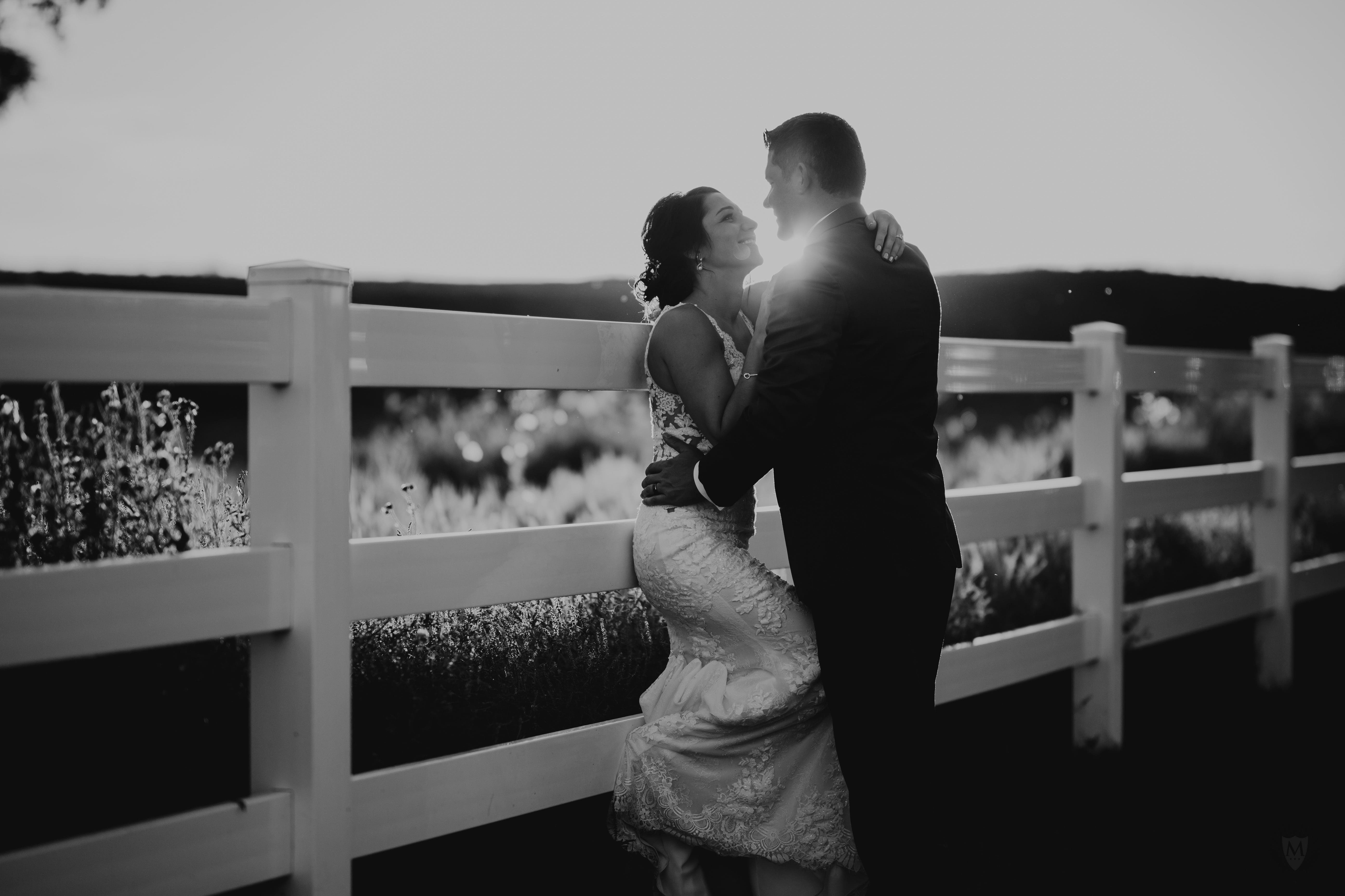 A bride and groom sharing a romantic kiss in front of a charming white fence captured beautifully by a skilled Sioux Falls photographer.