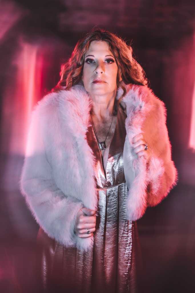 A woman in a fur coat posing in a dark room.