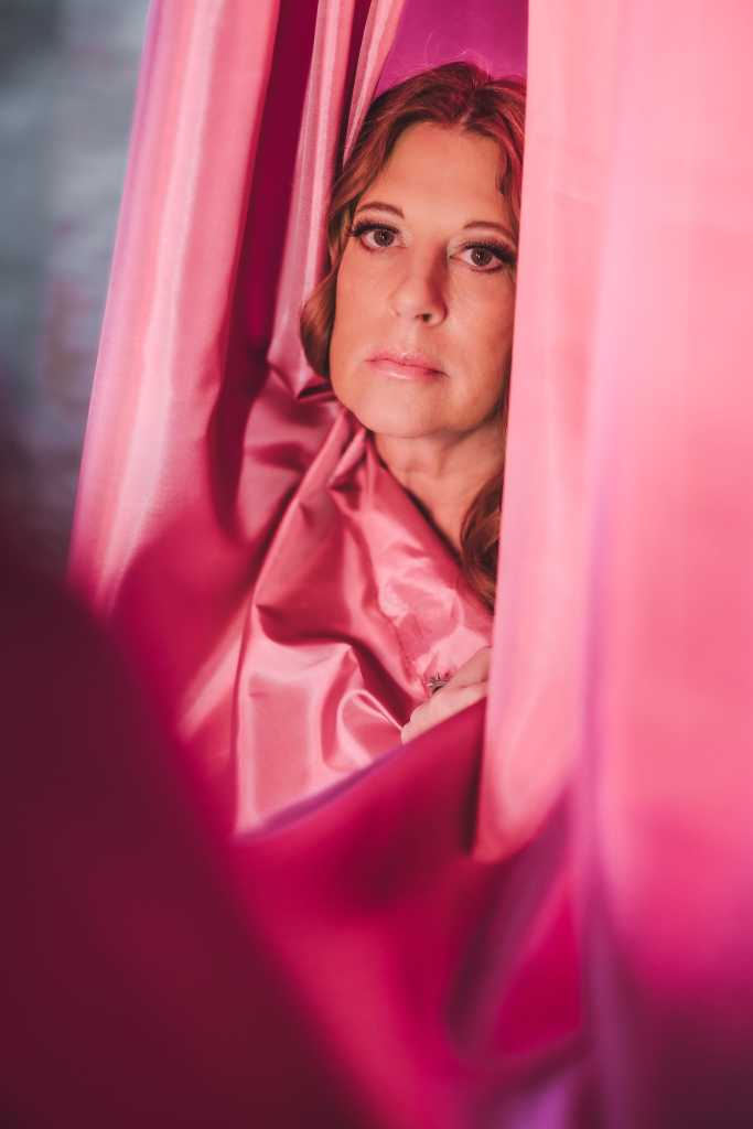 A woman is hiding behind a pink curtain.