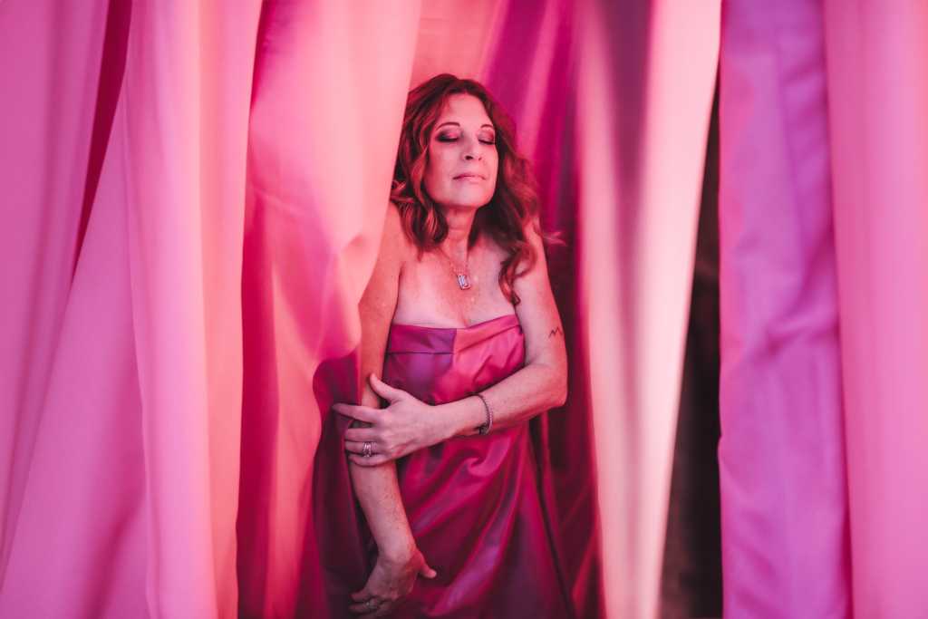 A woman in a pink dress standing behind a curtain.